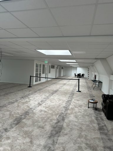 Lege gang met tapijt, verlichte ruimte en zitplaatsen aan het einde.